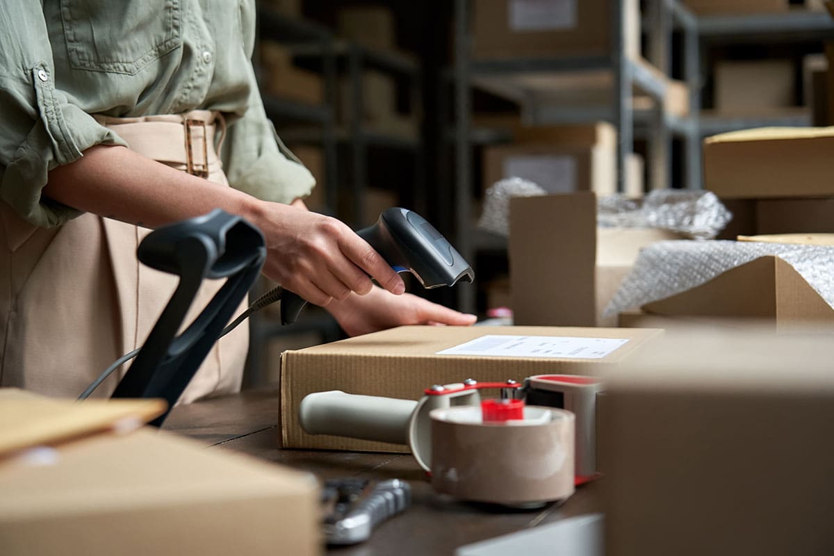 a lady scanning a box that needs to be sent for delivery for a logistics company with tons of boxes around her
