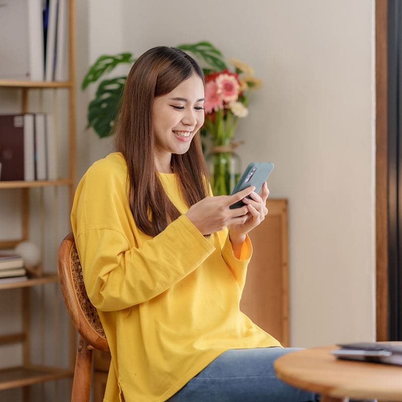 A woman smiling at her phone and working with a yellow sweater on