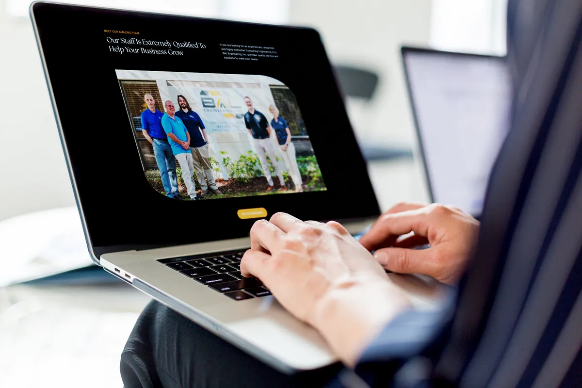 Person viewing a business website on a laptop, showcasing a team photo with the headline “Our Staff Is Extremely Qualified To Help Your Business Grow.