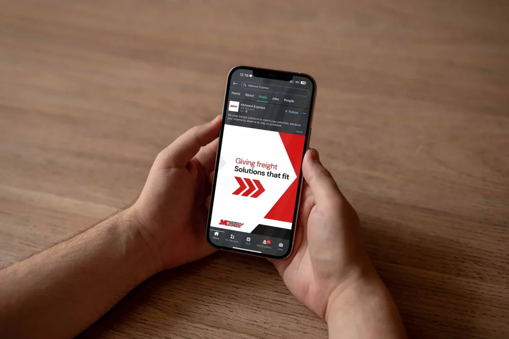 Person holding a smartphone displaying a Midwest Express social media post about freight solutions