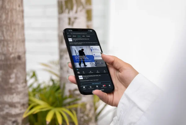 Hand holding a smartphone displaying a LinkedIn post for Preferred Building Services outdoors
