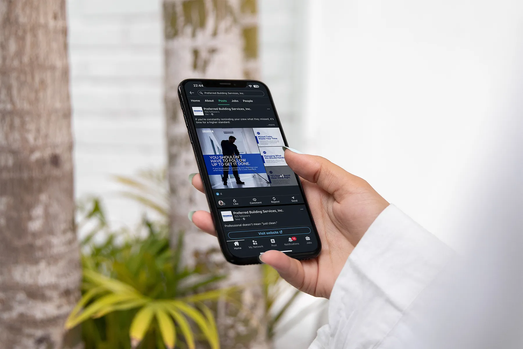 Hand holding a smartphone displaying a LinkedIn post for Preferred Building Services outdoors