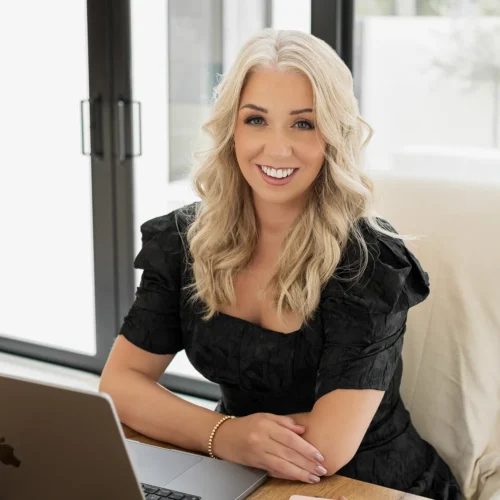 Lauren seated at desk smiling beside laptop and notebook in bright workspace