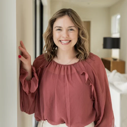 Maddie standing indoors smiling at camera with hand resting against wall