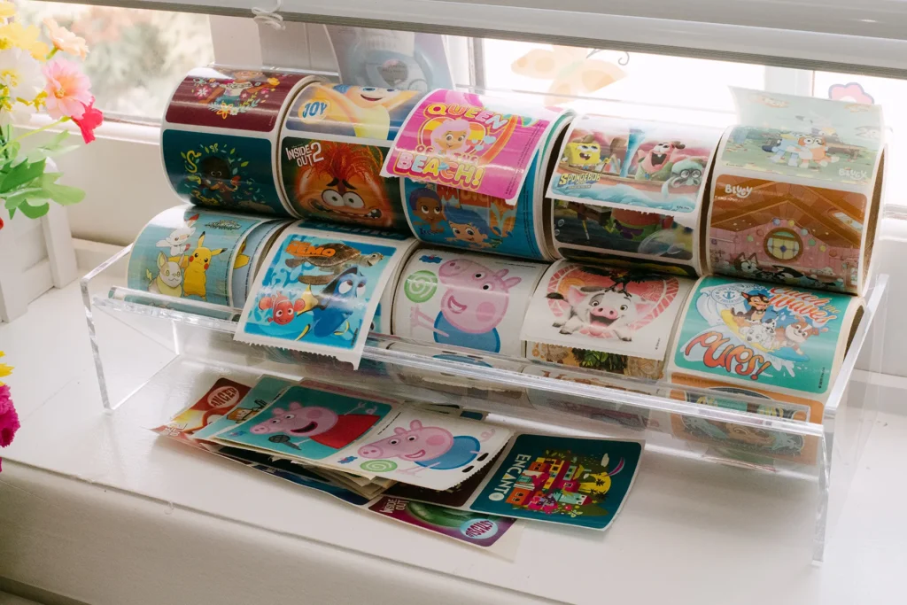 Colorful Kids’ Stickers Displayed in Pediatric Office A clear display filled with rolls of colorful children’s stickers featuring popular cartoon characters, sitting on a windowsill in a pediatric clinic.