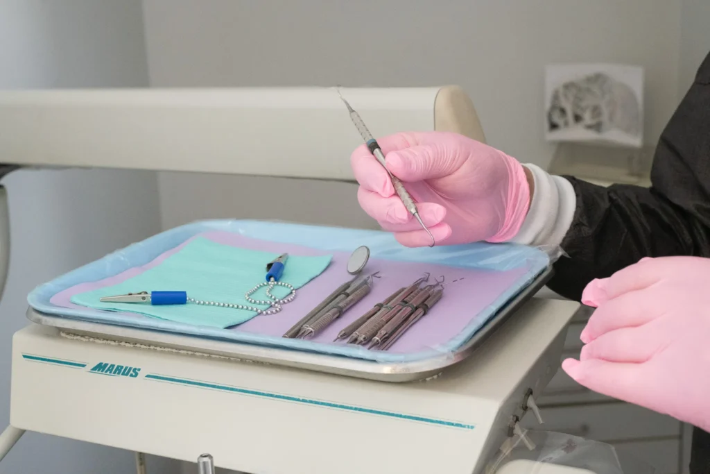 Dental Instruments Prepared for Pediatric Dental Treatment Close up of pink gloved hands holding a dental scaler above a tray of sterilized dental instruments in a pediatric dental office