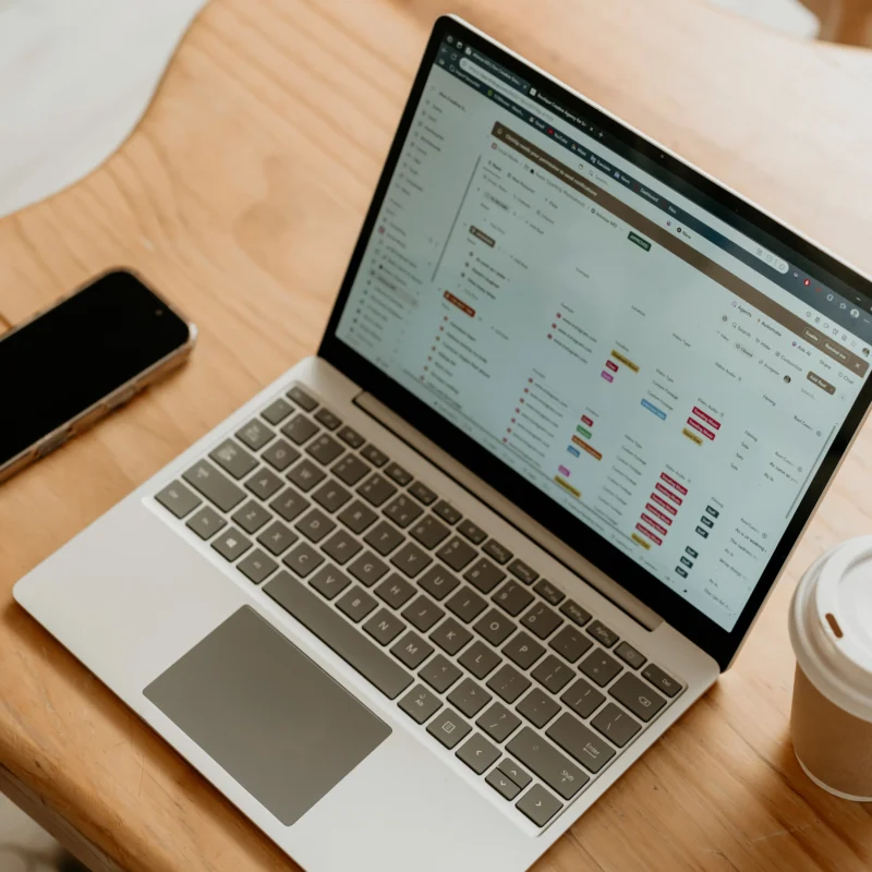 Laptop displaying project management dashboard on a wooden table with phone and coffee