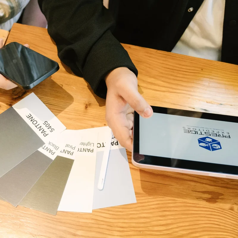 Hands reviewing brand design materials, including color swatches and a tablet displaying a logo, during a brand identity planning session.