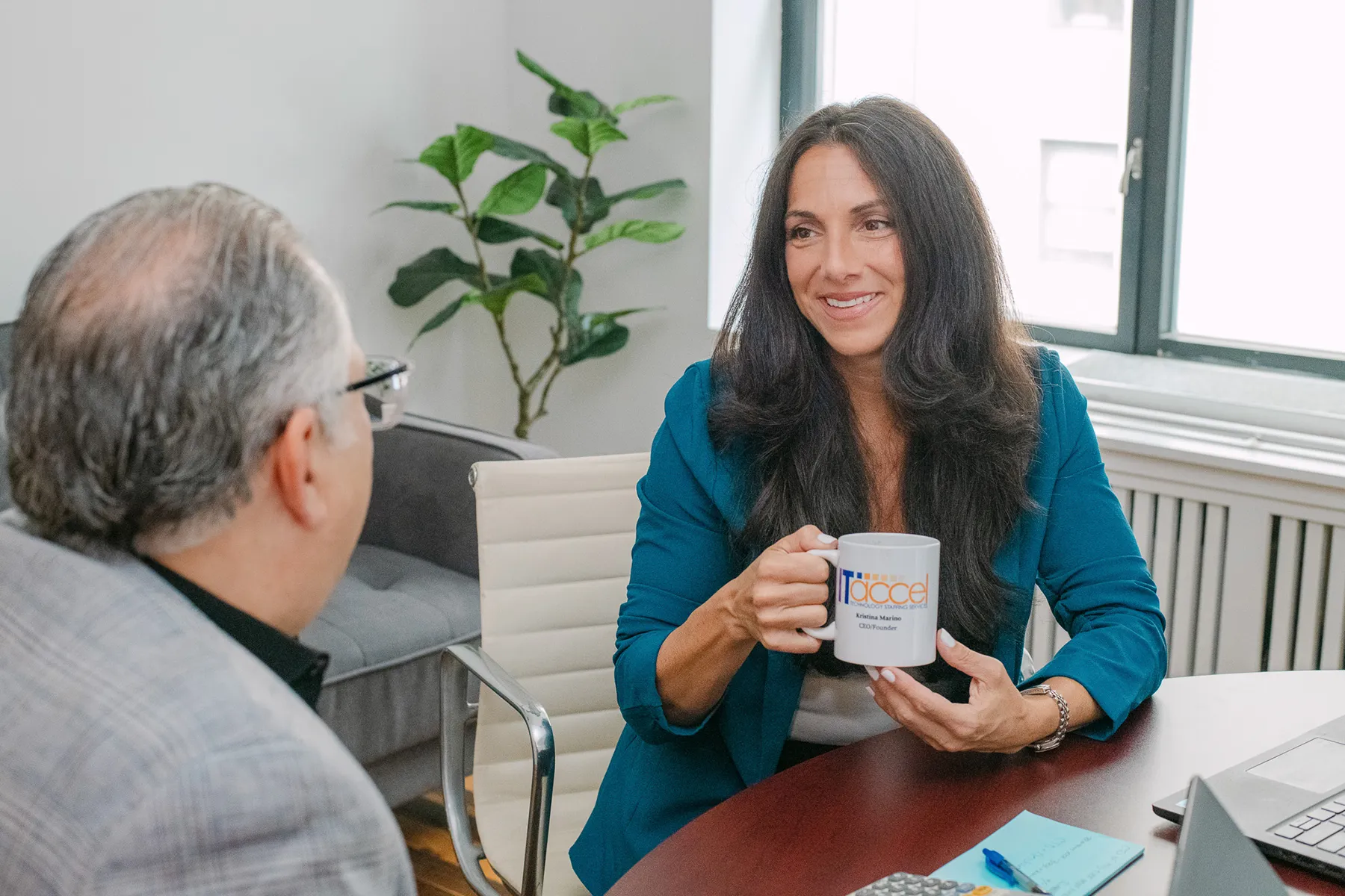 ITAccel consultant holding branded mug while meeting with client at office table