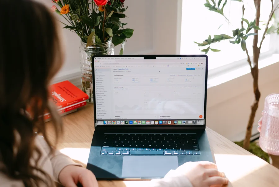 Person reviewing SEO analytics and keyword performance dashboard on a laptop at a home office desk with flowers and books.
