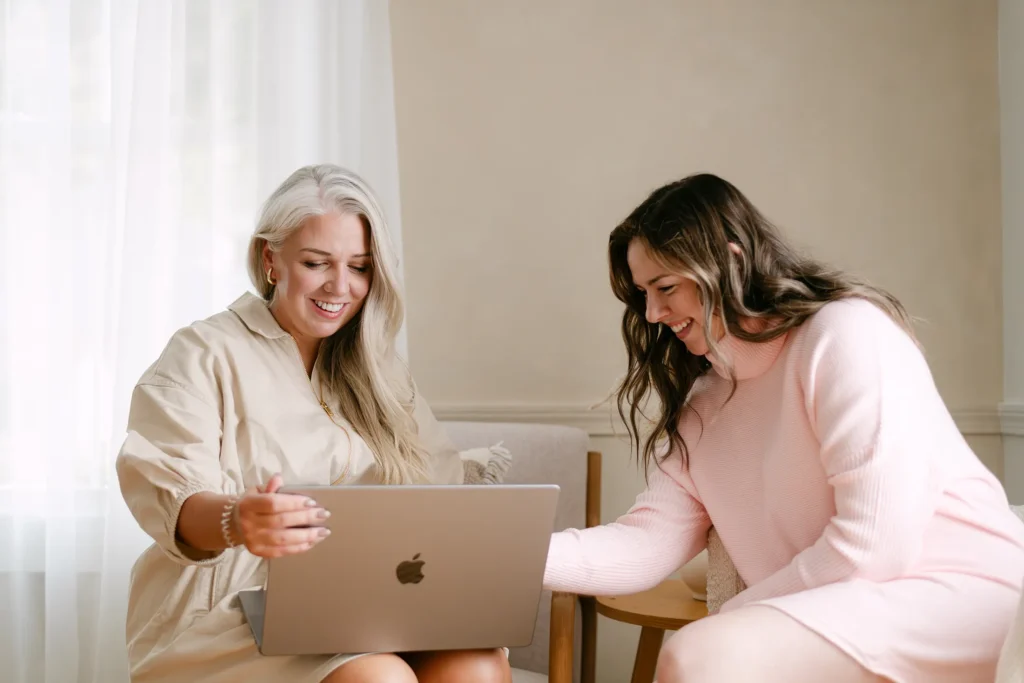 Two women reviewing marketing content on a laptop during a collaborative strategy meeting in a bright, modern workspace.