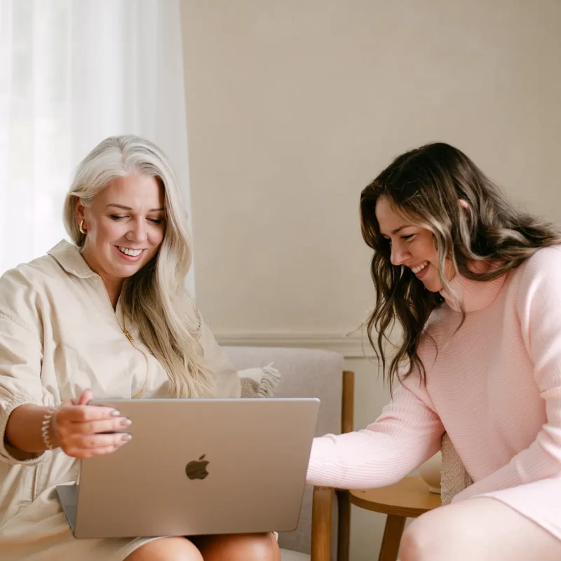 Two women reviewing marketing content on a laptop during a collaborative strategy meeting in a bright, modern workspace.