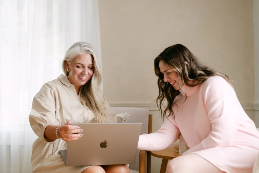 Two women reviewing marketing content on a laptop during a collaborative strategy meeting in a bright, modern workspace.