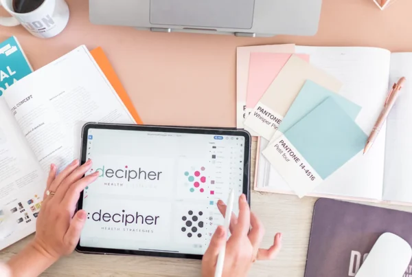 Designer reviewing Decipher Health logo concepts on tablet beside color swatches and notebooks