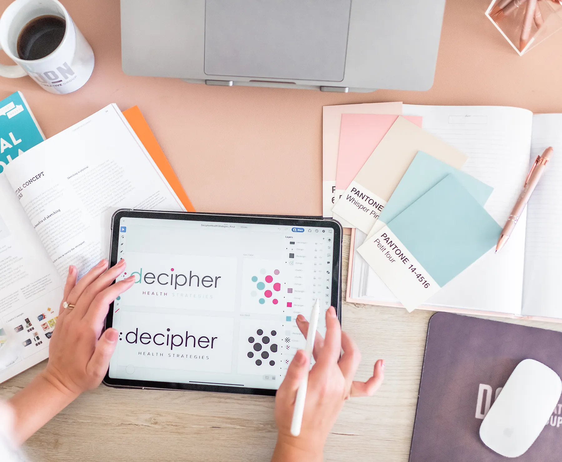 Designer reviewing Decipher Health logo concepts on tablet beside color swatches and notebooks