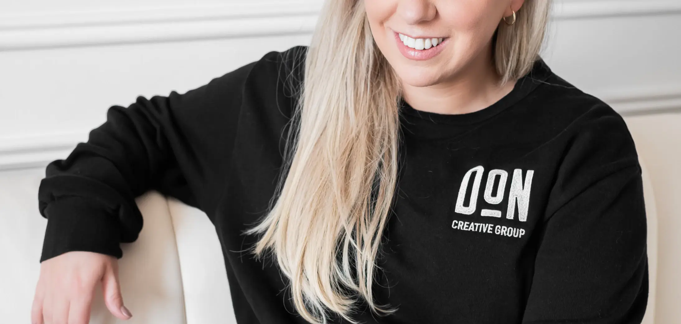 Team member wearing black Don Creative Group sweatshirt, seated indoors and smiling