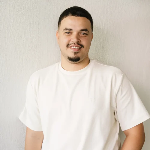 Douglas standing against light wall smiling at camera wearing white shirt