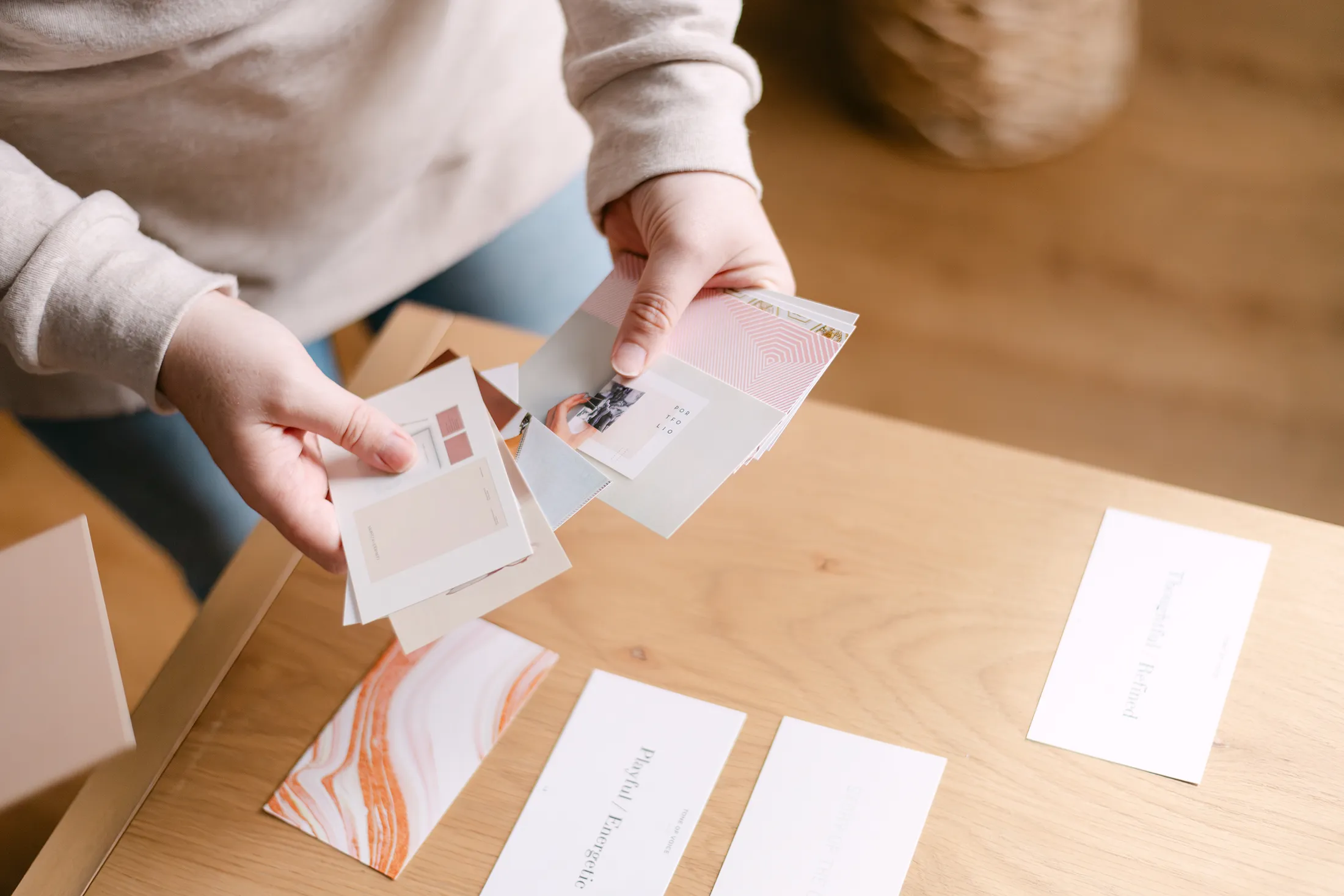 Hands sorting printed brand cards and design samples on wooden table