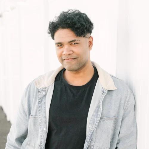 Team member wearing black shirt and denim jacket standing against white wall