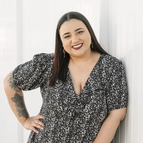 Team member smiling while standing against white wall wearing patterned black dress