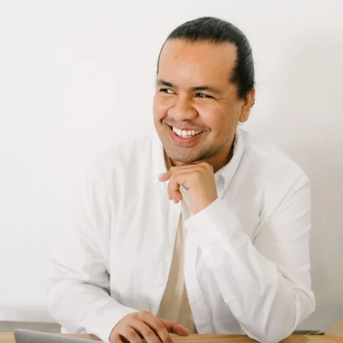 Team member in white shirt smiling while seated at desk with laptop