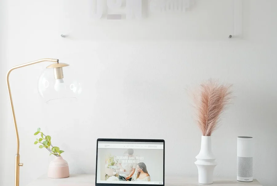 Minimalist office workspace with a laptop on a desk, soft pink chair, desk lamp, decorative plants, and a Don Creative Group wall sign in the background.
