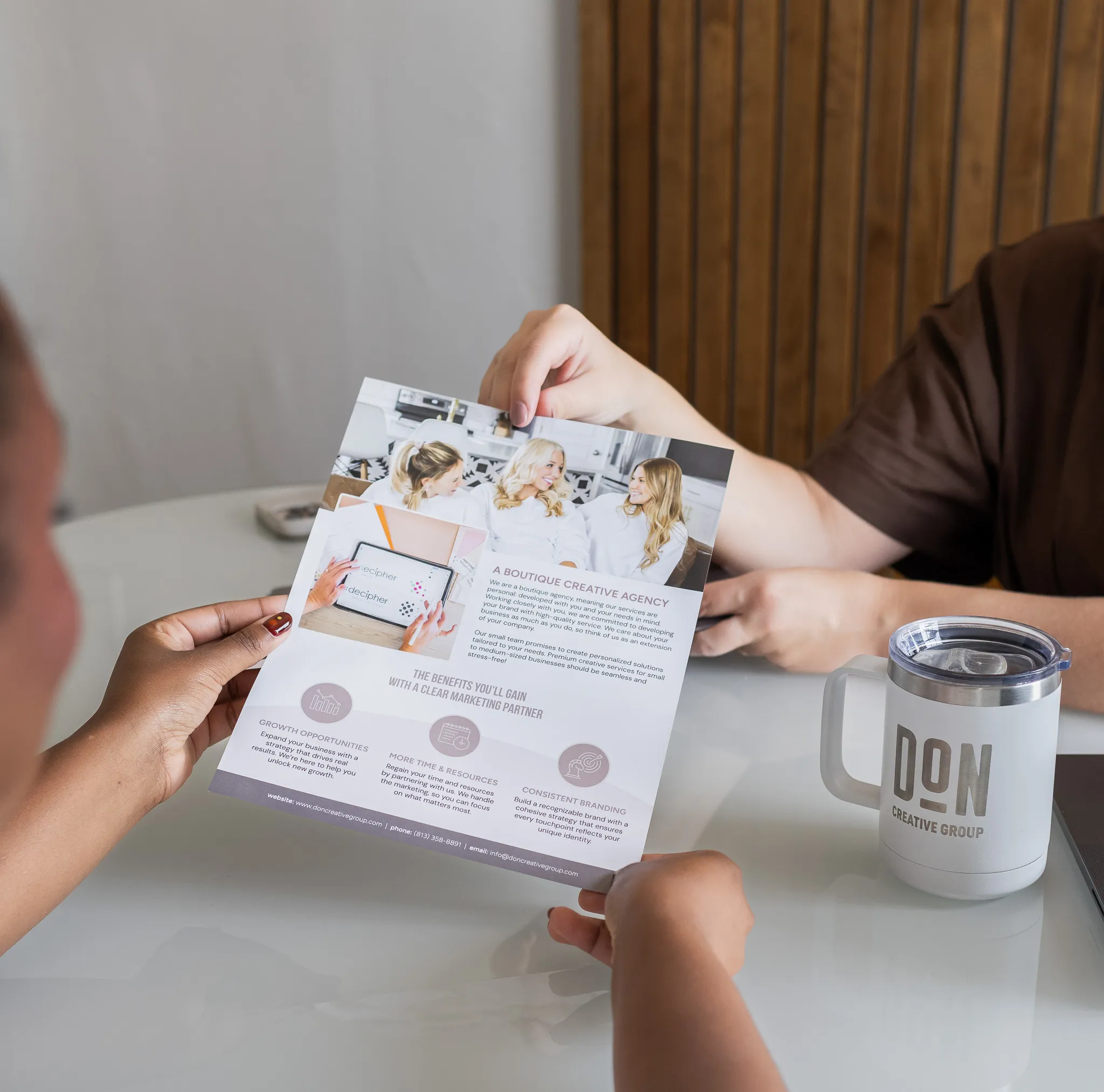 Two people reviewing a Don Creative Group marketing brochure at a table, highlighting creative agency services and branding benefits.