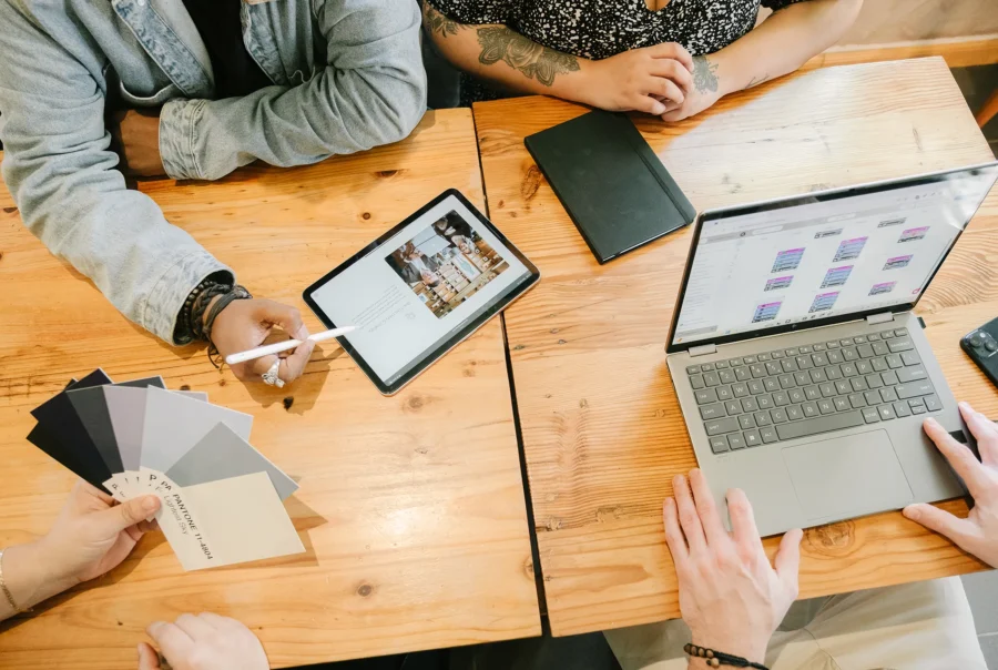 Team collaborating at a wooden table with a tablet displaying a website layout, a laptop showing content planning, and Pantone color swatches used for brand identity and rebranding work.